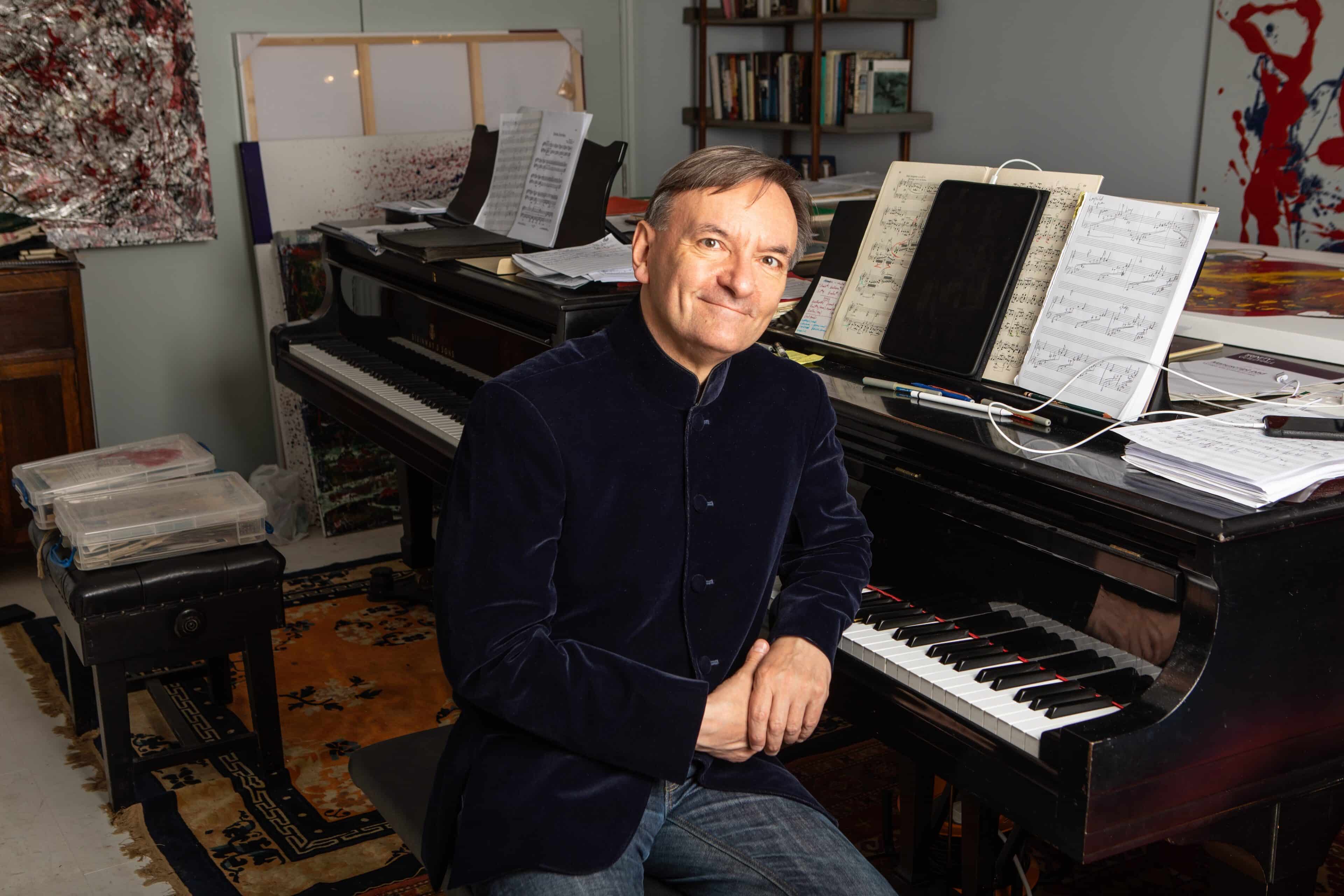 Photo of Sir Stephen Hough sat at a piano in either a piano study or an office