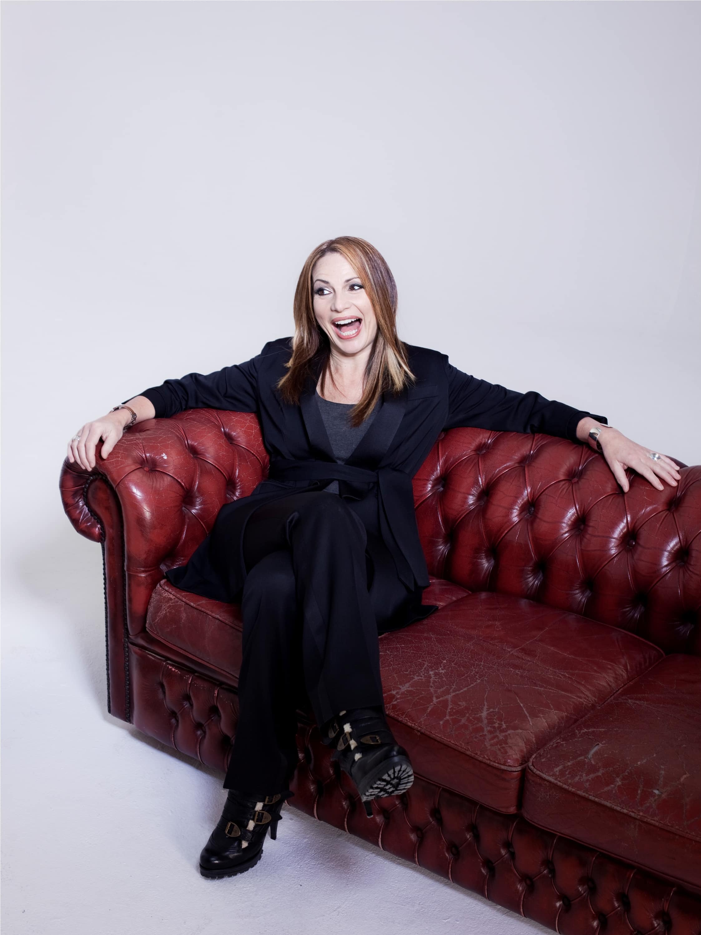Photo of Joanna sitting on a red sofa and smiling at something off-camera